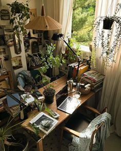 a desk with books, plants and pictures on it in front of a large window