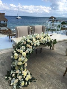 a long table with flowers on it in front of the ocean and chairs around it