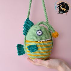 a hand holding a crocheted green and yellow purse with an evil fish on it