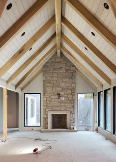 an empty living room with large windows and a stone fireplace in the center, surrounded by wood beams