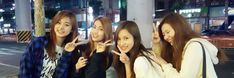 four young women standing next to each other in front of a street sign at night