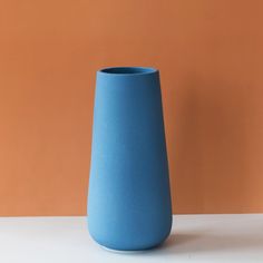 a blue vase sitting on top of a white table next to an orange and brown wall