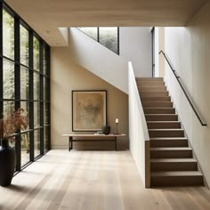 a staircase leading up to a living room with large windows and wooden flooring on both sides