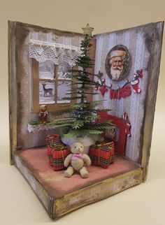 there is a small christmas tree in an open book with a teddy bear next to it