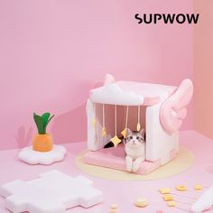 a cat sitting in a pink play house surrounded by other toys and decorations on a table