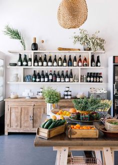 an assortment of fruits and vegetables on a table in a room with shelves full of bottles