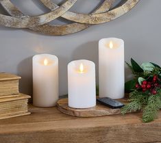 three white candles sitting on top of a wooden table next to a cell phone and christmas greenery