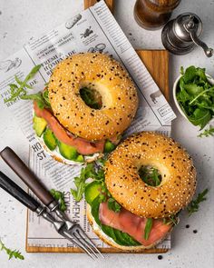 two bagels with ham and lettuce on them sitting on a cutting board