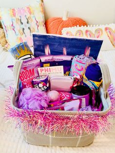 a basket filled with lots of items on top of a white bed covered in pink tinsel