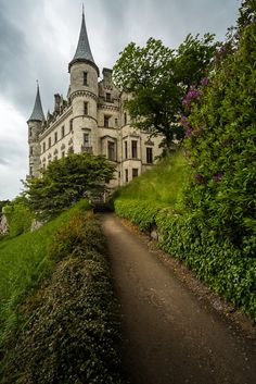 an old castle sitting on top of a lush green hillside next to a dirt road