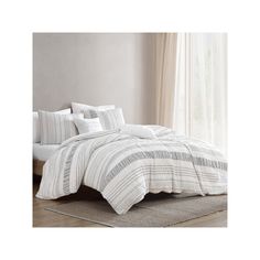 a bed with white and grey striped comforter on top of it in front of a window