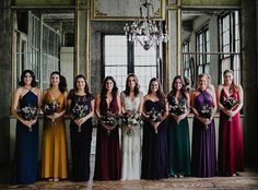 a group of women standing next to each other holding bouquets in front of a chandelier