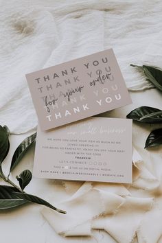 a thank you card sitting on top of a white blanket next to some green leaves