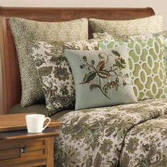 a bed with green and brown pillows on top of it next to a night stand