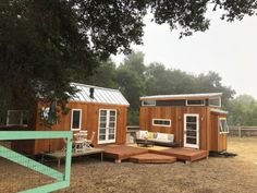 two tiny houses sitting in the middle of a field next to a fence and trees