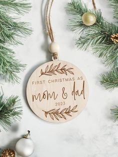 a wooden ornament hanging from a christmas tree with ornaments around it and the words, first christmas as mom & dad