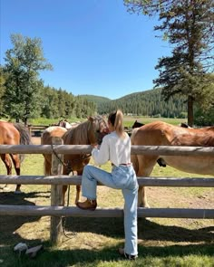 a woman sitting on a fence with horses in the background