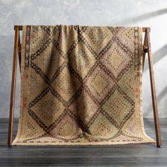 an old rug is hanging on a wooden stand in front of a gray wall and wood floor