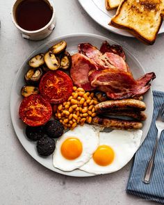 a plate with eggs, bacon, beans and toast on it next to a cup of coffee