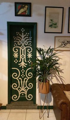 a potted plant sitting next to a green door in a room with pictures on the wall