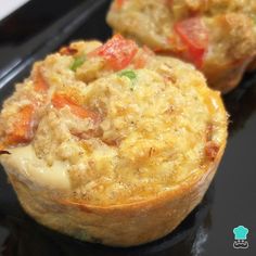 two muffins with cheese and vegetables in them on a black tray, ready to be eaten