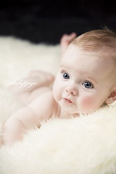 a baby laying on top of a fluffy white blanket looking at the camera with blue eyes