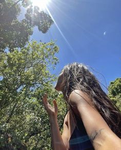 a woman standing in front of trees with her hand up to the sky and sun shining on her face