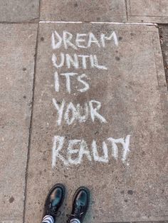 someone's feet standing on the sidewalk with chalk writing in front of them that says dream until it's your reality