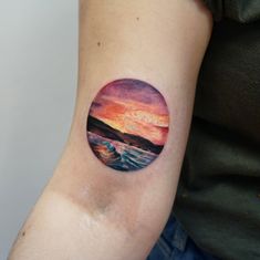 a woman's arm with a sunset and wave tattoo on the left side of her arm