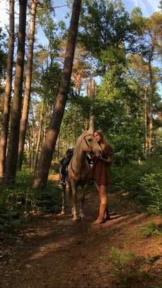 a woman is standing next to a horse on a trail in the woods with trees