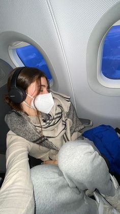 a woman wearing headphones while sitting in an airplane seat with her face mask on