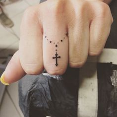 a person with a small cross tattoo on their thumb and finger, holding onto a bar