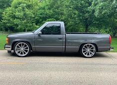 a silver truck parked on the side of a road in front of some green trees