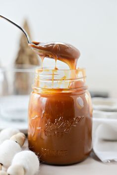 a spoon full of caramel sauce with marshmallows on the table next to it