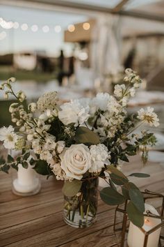 a vase filled with white flowers sitting on top of a wooden table next to a candle