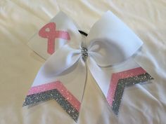 a white bow with pink and silver glitters on it sitting on top of a bed