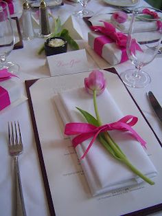 the table is set with napkins, silverware and pink tulips on them