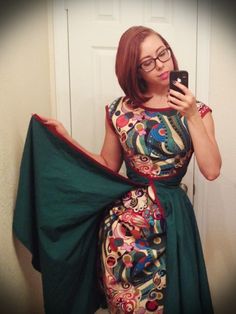 a woman in a dress taking a selfie with her cell phone while wearing glasses