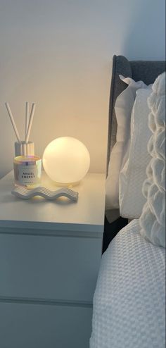 a white night light sitting on top of a nightstand next to a pillow and bed