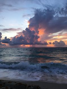 the sun is setting over the ocean with clouds in the sky and waves on the beach