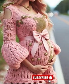 a pregnant woman wearing a pink knitted dress and holding her belly in the air