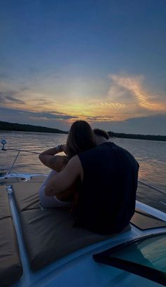 two people sitting on the back of a boat at sunset