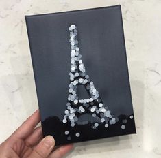 a hand holding up an acrylic canvas with the eiffel tower painted on it