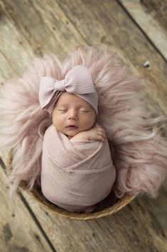 a newborn baby is wrapped up in a pink wrap and wearing a bow on her head