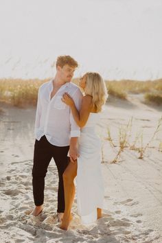 a man and woman standing on top of a sandy beach