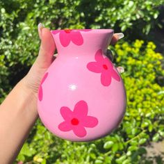 a hand holding a pink vase with flowers painted on it