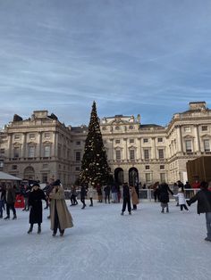 people walking around in the snow near a large building with a christmas tree on it