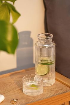 two glasses sitting on top of a wooden table next to a vase with green leaves