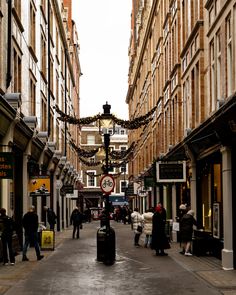 people are walking down the street in an old european city with shops and stores on both sides