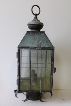 an old fashioned lantern is sitting on a table with a white wall in the background